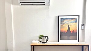 Una kitchenette pequeña con refrigerador, cafetera y un cuadro enmarcado de un atardecer sobre un templo.
