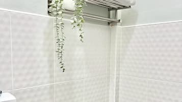 Un baño con inodoro, secamanos, repisa con toallas y una planta colgante.