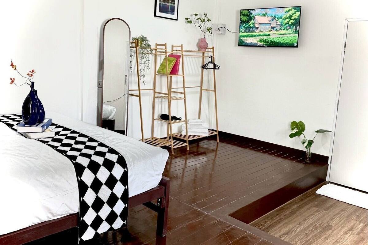 A bedroom with a bed, a wooden ladder shelf, a television, and a painting on the wall.