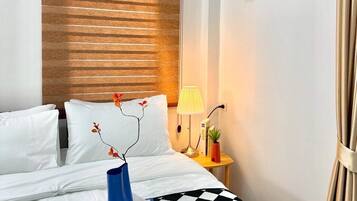 A hotel room with a bed, a nightstand, a lamp, a framed picture on the wall, and a window with blinds.