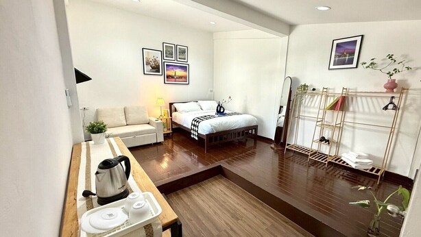 Habitación de hotel compacta con cama, mesita de noche, lámpara y un pequeño rincón de descanso.