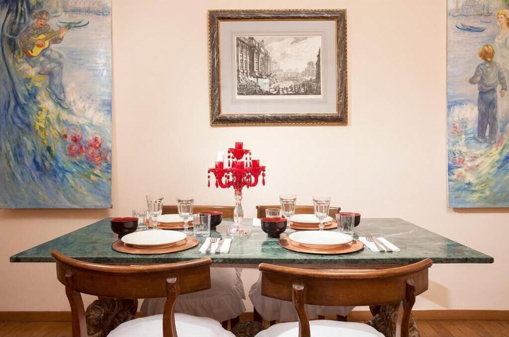 A dining table set with plates, glasses, and a red centerpiece.