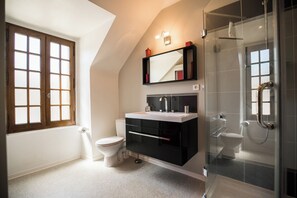 Ein modernes Badezimmer mit Duschkabine aus Glas, einer weißen Toilette und einem schwarzen Waschtisch mit Spiegel.