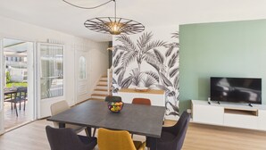 Un comedor con una mesa, sillas, un frutero, un televisor y una escalera.
