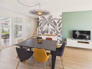 A dining area with a table, chairs, a fruit bowl, a TV, and a staircase. - 600m to the beach – House for 6 with veranda (Treffiagat)
