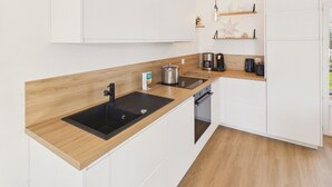 Una cocina moderna con armarios blancos, encimera de madera, un fregadero, una estufa y una cafetera.