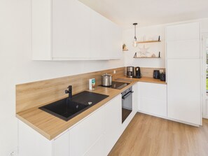 A modern kitchen with white cabinets, a wooden countertop, a sink, a stove, and a coffee maker. - 600m to the beach – House for 6 with veranda (Treffiagat)