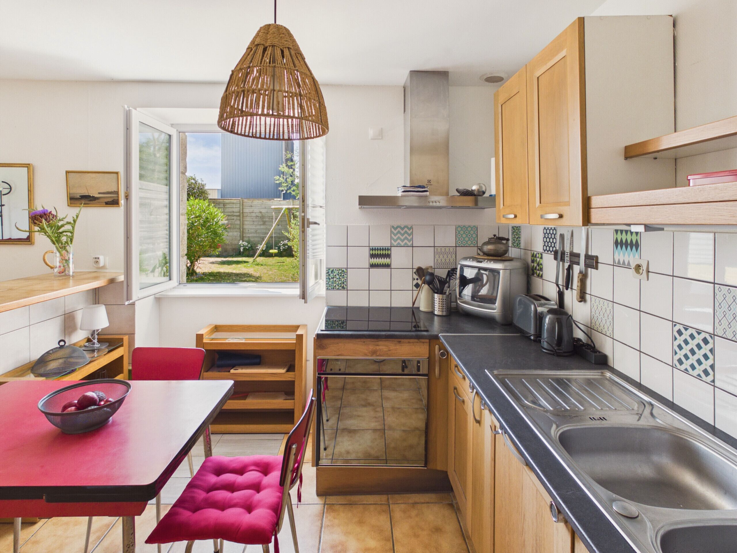 A kitchen with wooden cabinets, a black countertop, a sink, a toaster, and a hanging light fixture.