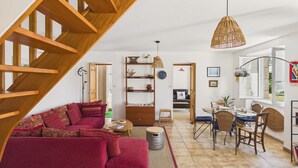 A spacious living area with a wooden staircase, a red sofa, a dining table with chairs, and a bookshelf. - Family home for 5, garden - La Torche (Plomeur)