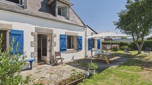 A two-story house with a stone facade, blue shutters, and a small patio with a table and chairs. - Family home for 5, garden - La Torche (Plomeur)