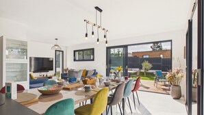 A modern living room with a TV, sofa, and dining area. - Superb recently built house for 8 with garden (Pléneuf-Val-André)