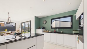A modern kitchen with a large island, white cabinetry, a green accent wall, and a window above the sink. - Superb recently built house for 8 with garden (Pléneuf-Val-André)