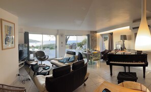 A spacious living area with a piano, seating, and a view of the sea. - House right on the beach in Arzon Port Navalo (Arzon)
