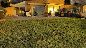 A house with a large glass door entrance, a patio with outdoor furniture, and a well-maintained lawn. - House Ocean Front Arzon Port Navalo (Arzon)