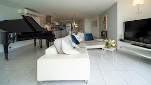 A modern living room with a grand piano, a large flat-screen TV, a white sofa, and a small table with a vase of flowers. - House Ocean Front Arzon Port Navalo (Arzon)