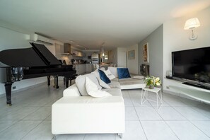 Un salon moderne avec un grand piano, un téléviseur à écran plat, un canapé blanc et une petite table sur laquelle est posé un vase de fleurs.