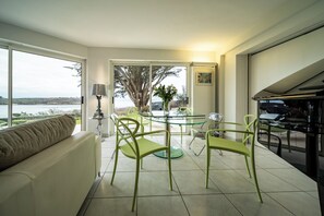 A modern living space with a glass dining table, green chairs, a sofa with a cushion, a lamp, and a view of the outdoors. - House Ocean Front Arzon Port Navalo (Arzon)