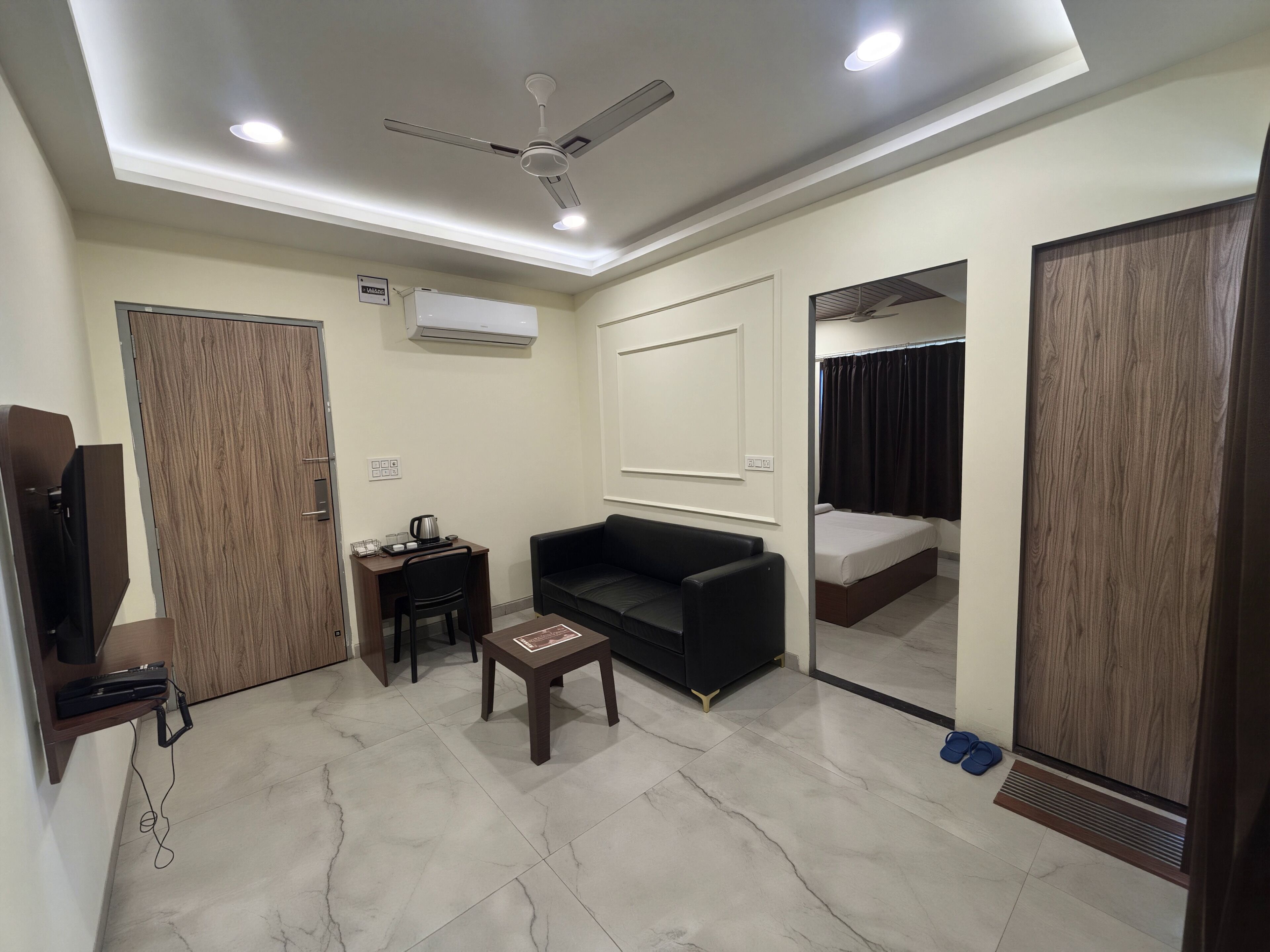 A modern hotel room with a ceiling fan, a desk with a chair, a black sofa, a small table, and a bed.