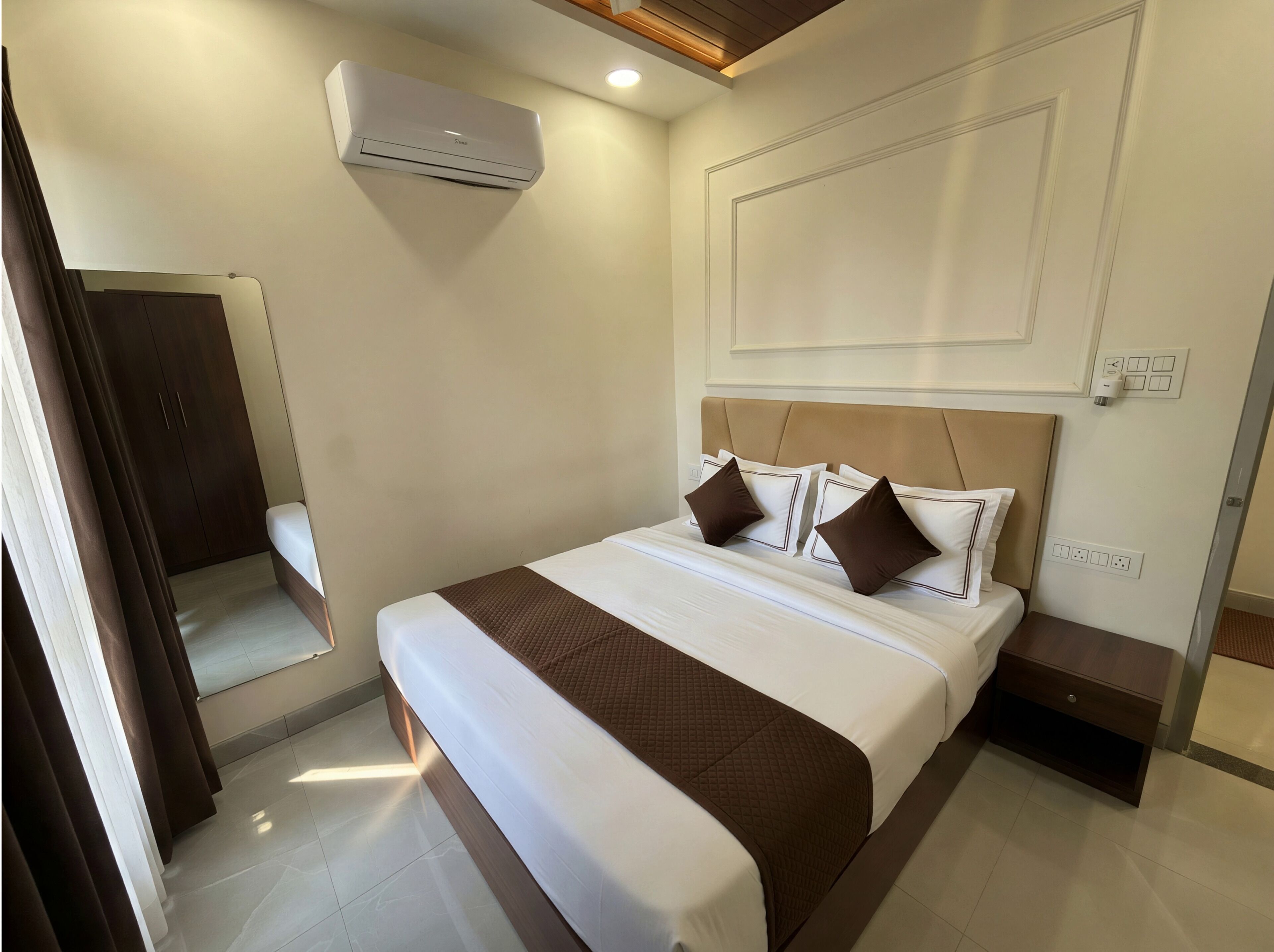 A hotel room with a bed, bedside tables, an air conditioning unit, a wardrobe, and a mirror.