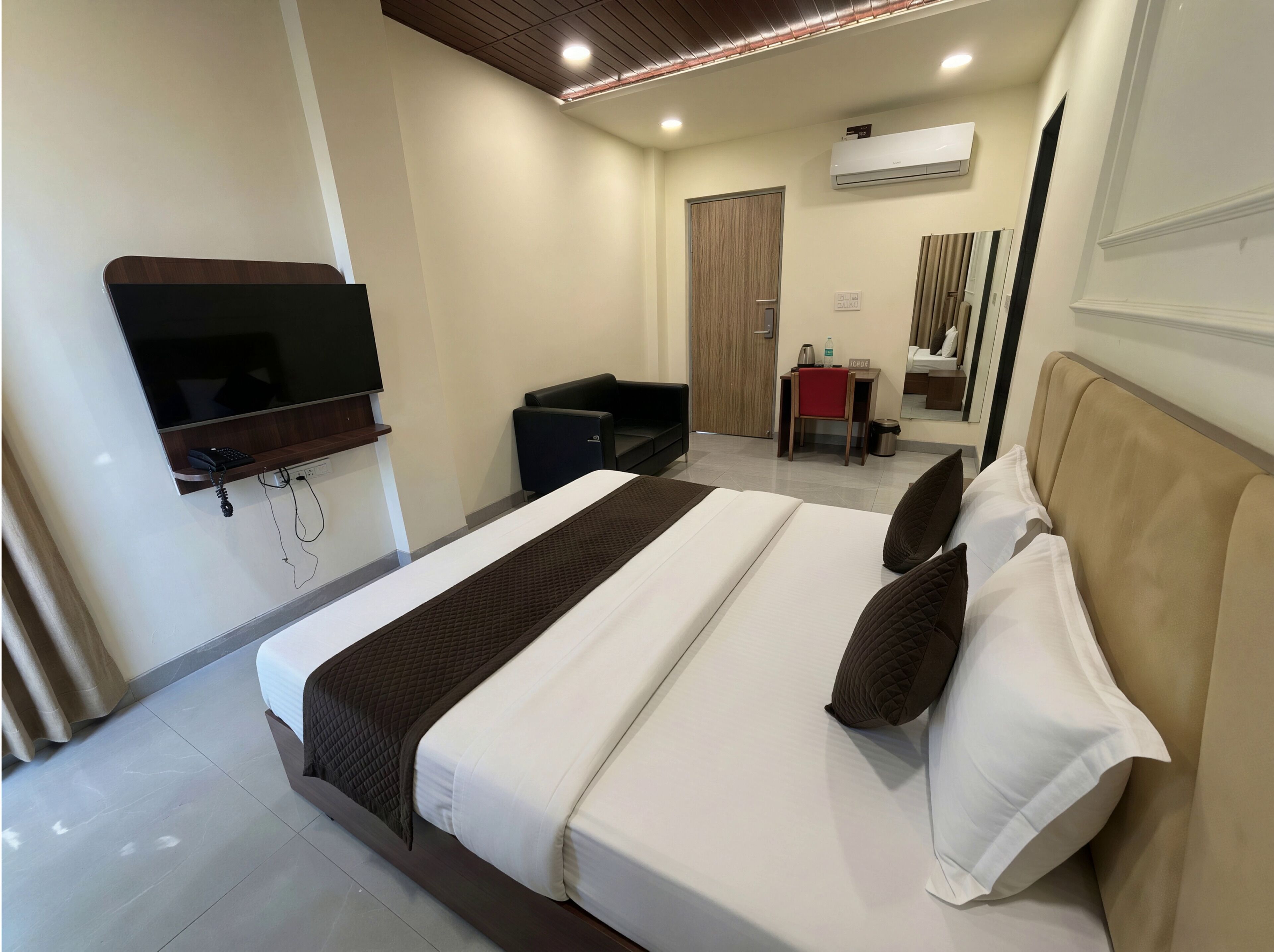 A hotel room with a bed, a desk, a chair, a television, and an air conditioning unit.