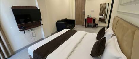 A hotel room with a bed, a desk, a chair, a television, and an air conditioning unit.