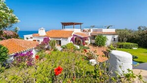Un edificio bianco con tetti in tegole rosse, una pergola e vista sul mare.