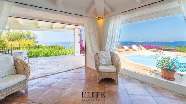 Un'area patio coperta con una sedia in vimini, un divano e vista sul mare e sulla piscina.
