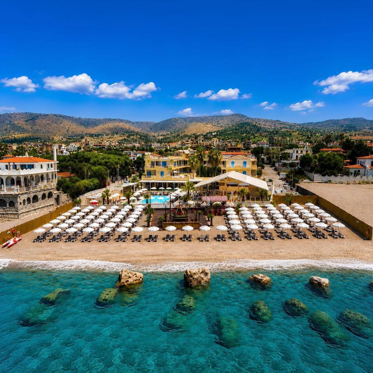 Un resort costero con piscina, sombrillas de playa y vistas a las montañas.