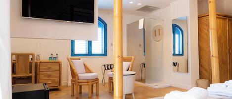 Una habitación de hotel moderna con cama, televisor, ducha y baño con espejo.