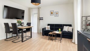 Een moderne woonkamer met een eetgedeelte, een zwarte bank, een televisie en een minimalistische inrichting.