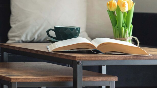 Een houten tafel met een open boek en een vaas gele tulpen.