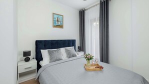 Een keurig opgemaakt slaapkamer met een bed, nachtkastjes, een schilderij en een dienblad met bloemen en glazen.
