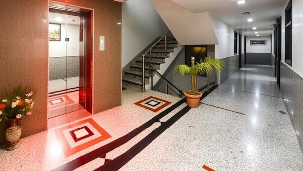 Un'elegante hall d'albergo con un ascensore in vetro, una scala e una pianta in vaso.