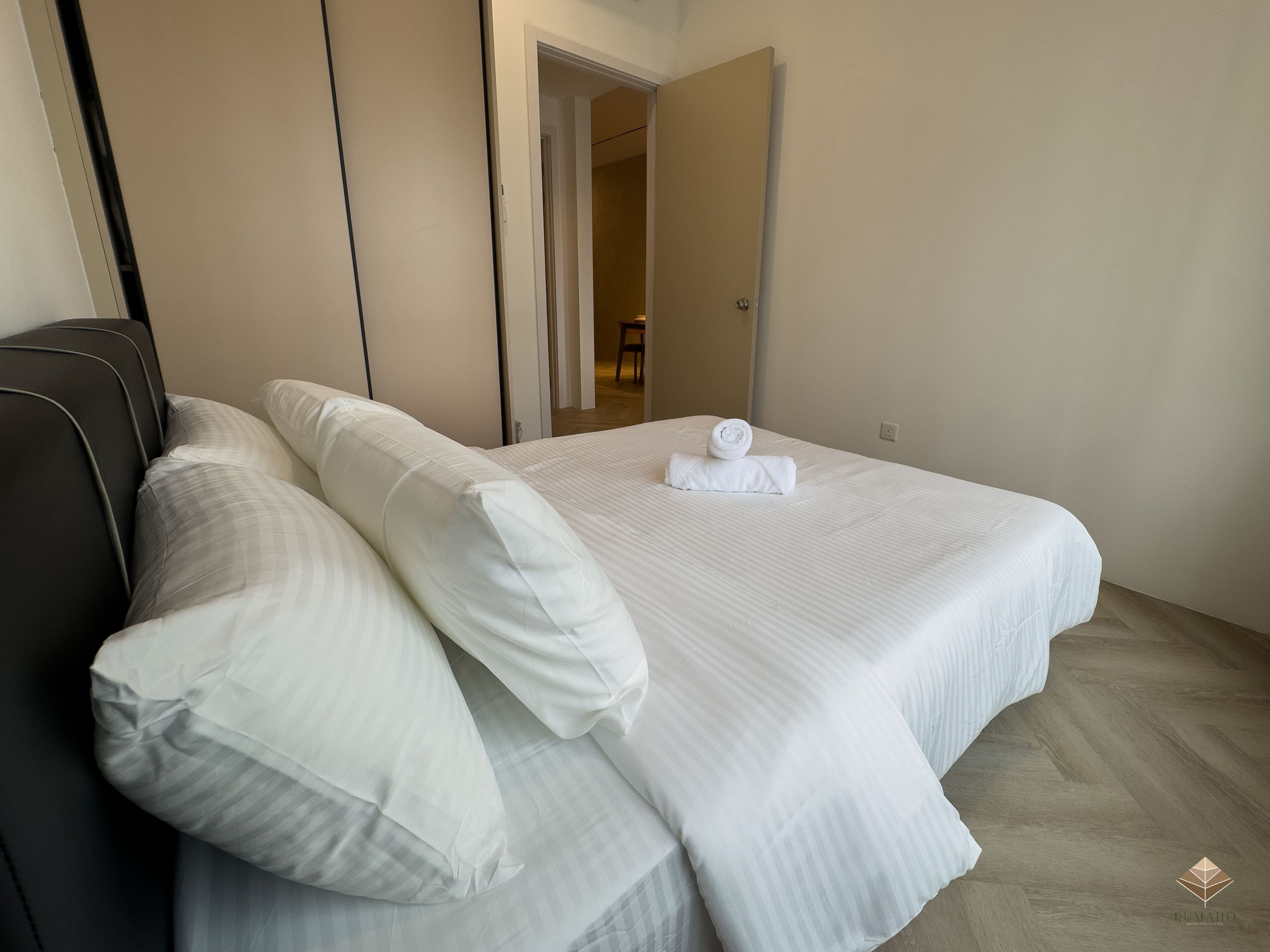 Un lit bien fait, avec du linge de lit blanc et des oreillers, une tête de lit sombre et un plancher en bois.