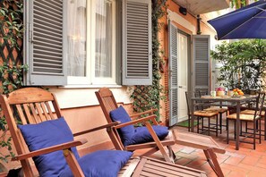 Eine Terrasse mit Holzkufen und einem Tisch, ein Fenster mit Rollläden und eine Tür.
