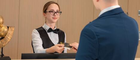 A reception desk with three clocks on the wall, a receptionist, and a guest.