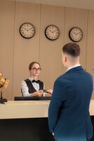 A reception desk with three clocks on the wall, a receptionist, and a guest.