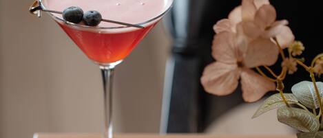 A martini glass with a pink drink, blueberries, and a flower on a table with a menu.