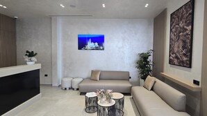 A modern reception area with a sofa, two round tables, a large framed picture, and a potted plant. - Koral Boutique Hotel & Bistro (Durrës)