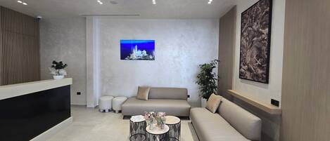 A modern reception area with a sofa, two round tables, a large framed picture, and a potted plant.