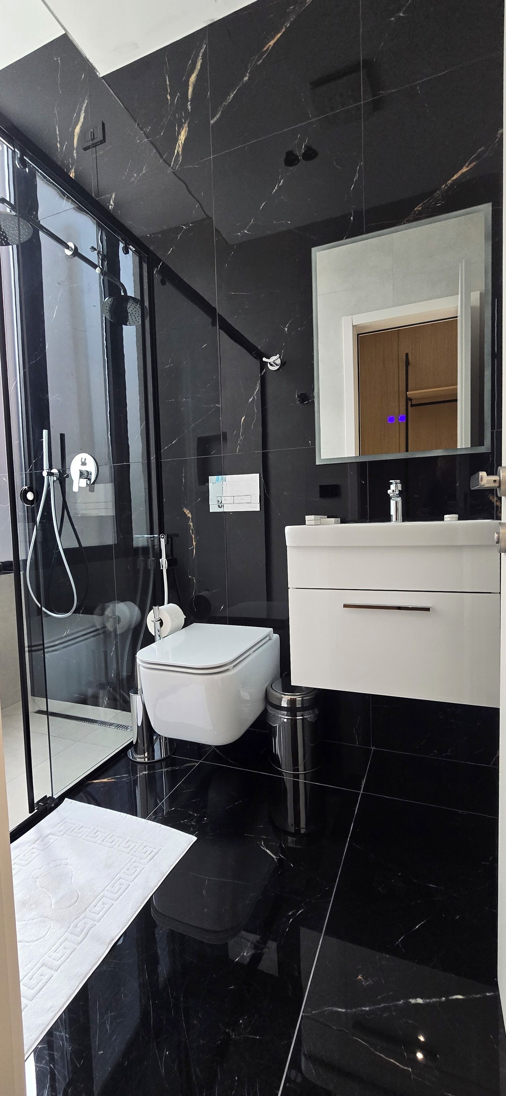 A modern bathroom with a glass shower enclosure, a white toilet, and a white vanity with a mirror.