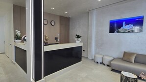 A reception desk with a modern design, a sofa, a small table, and a wall-mounted TV. - Koral Boutique Hotel & Bistro (Durrës)