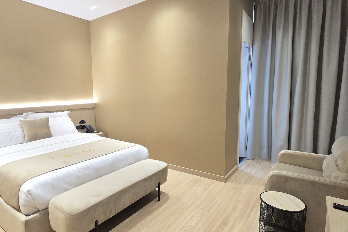 A hotel room with a bed, bedside table, lamp, and a seating area with a chair and a small table.