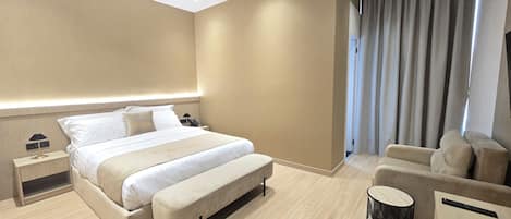 A hotel room with a bed, bedside table, lamp, and a seating area with a chair and a small table.