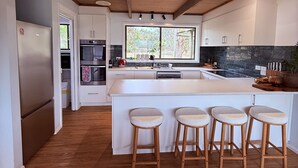A modern kitchen with a central island, bar stools, a large window, and wooden ceiling beams. - Southern Grampians Lookout (Dunkeld)