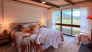A bedroom with a bed, nightstands, a ceiling fan, a large window with a view, and a chair. - Southern Grampians Lookout (Dunkeld)