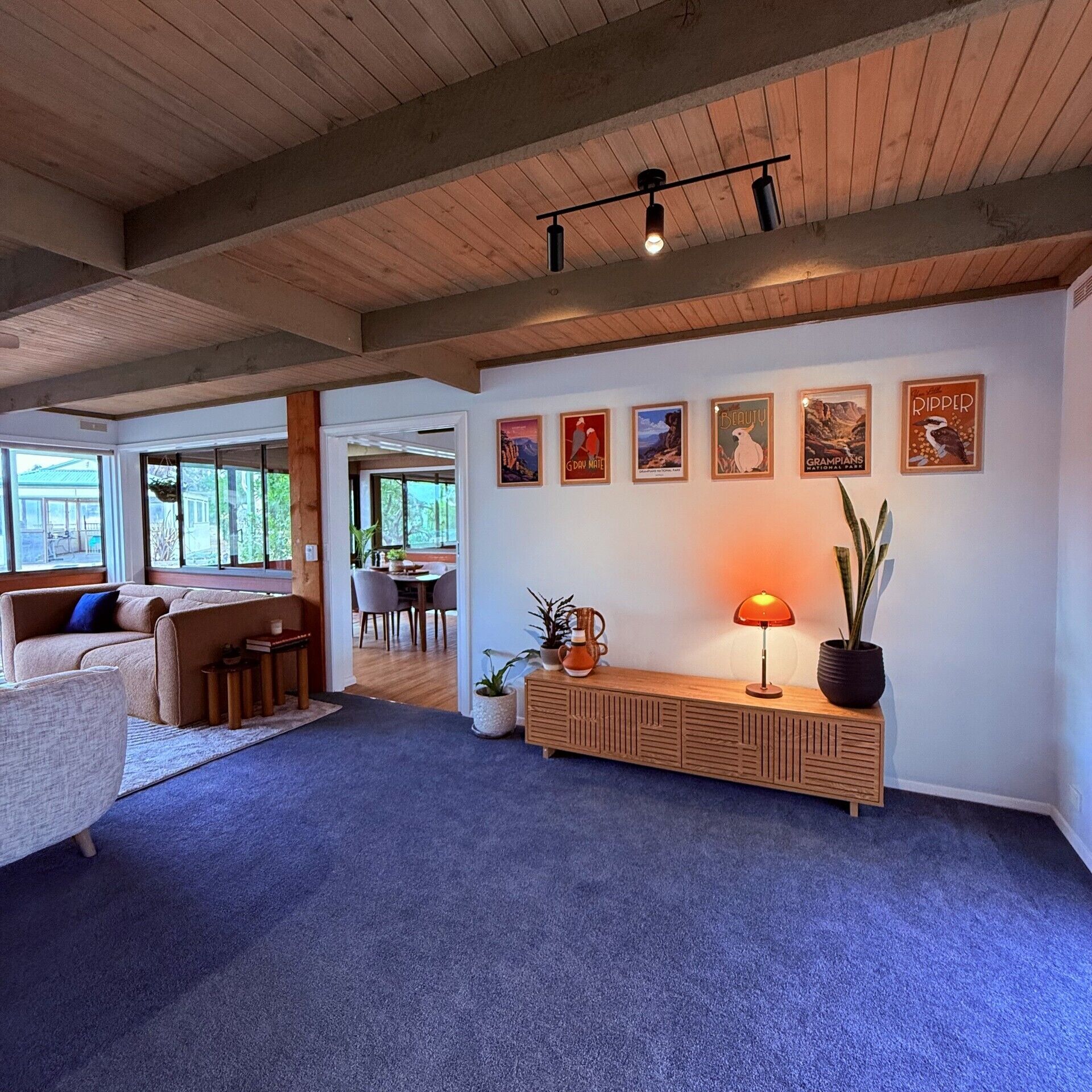 A spacious living area with a wooden ceiling, a sofa, a coffee table, a lamp, and wall art.