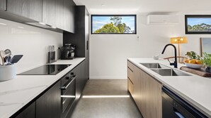 Une cuisine moderne avec des meubles de couleur sombre, une grande fenêtre et une vue sur les arbres.