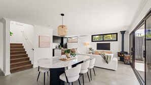 Un intérieur moderne comprenant un coin repas, un canapé, un escalier et une vue sur l’extérieur à travers une porte vitrée.