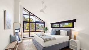 Une chambre avec une grande fenêtre, un lit, une table de chevet, un miroir et un banc.